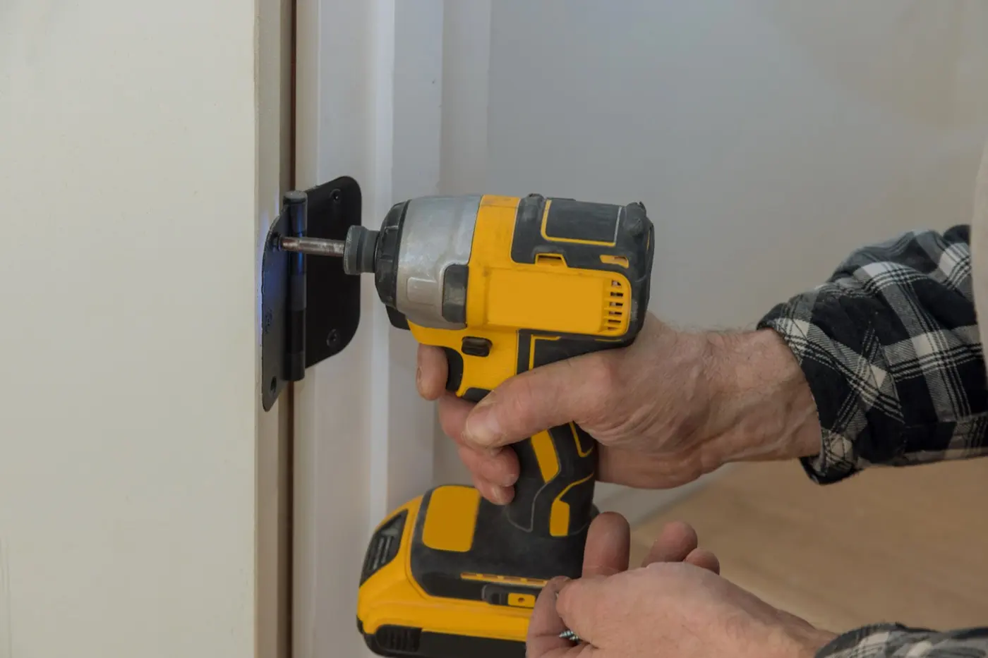Hands adjusting a door hinge with a drill driver