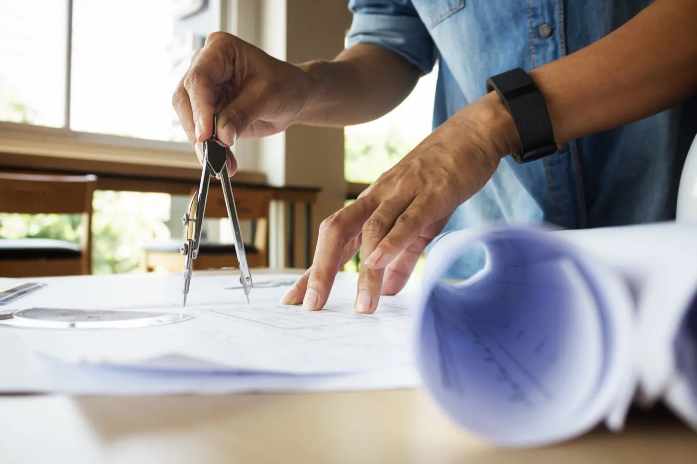 Hands measuring a blueprint with a drafting compass