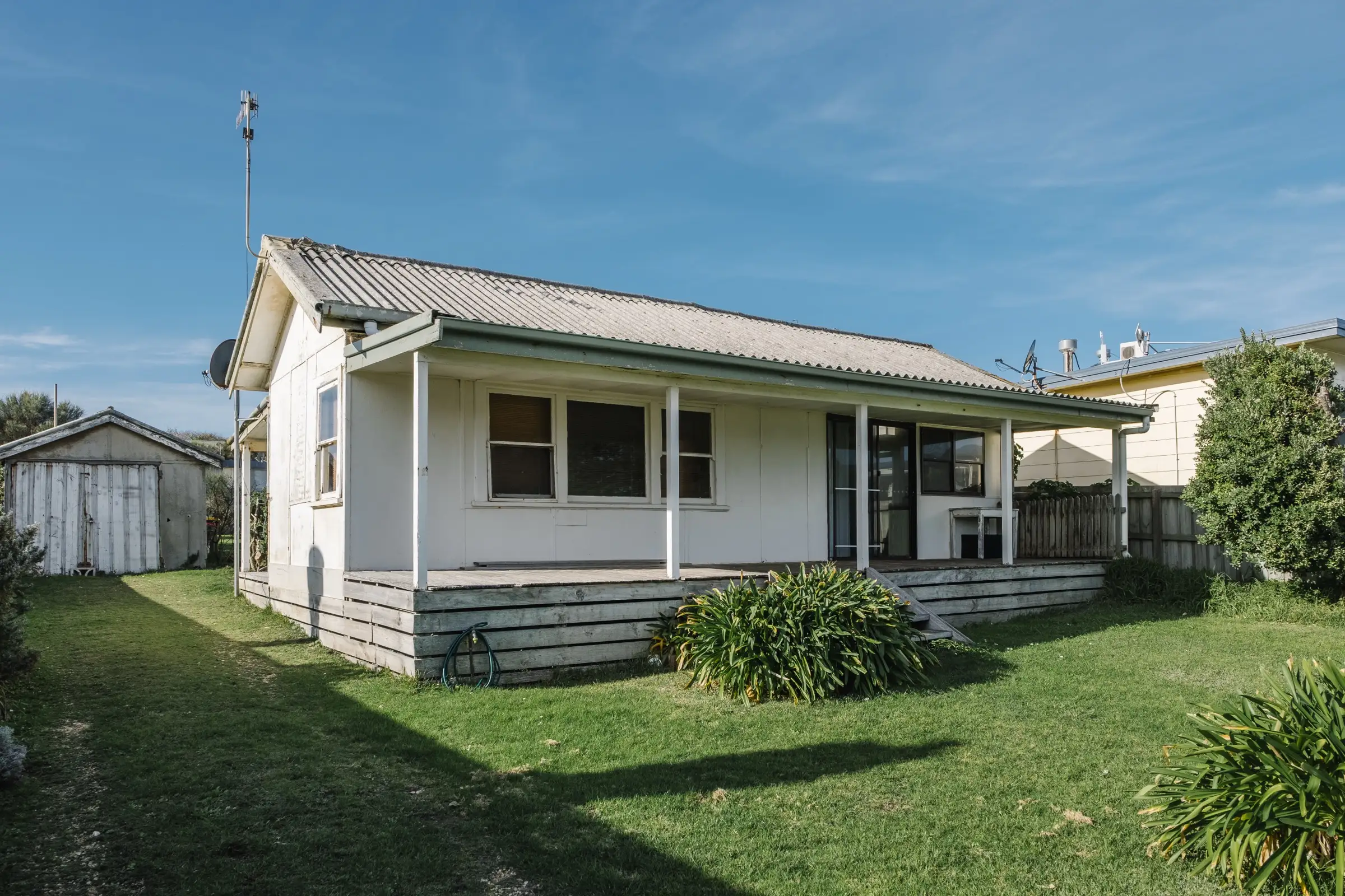 Small white frame house with a porch, raised above the lawn